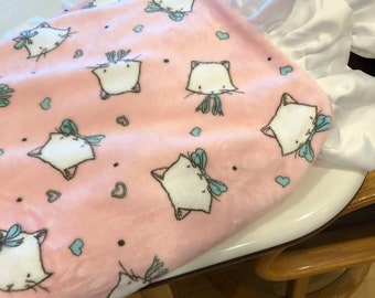 A blanket  in a pink kitty print, it has a white dimple dot packing