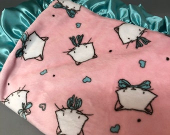 A blanket  in a pink kitty print, it has a white dimple dot packing