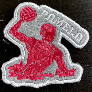 May include: A grey and pink embroidered patch featuring a silhouette of a person playing water polo. The patch is labelled "Pamela".