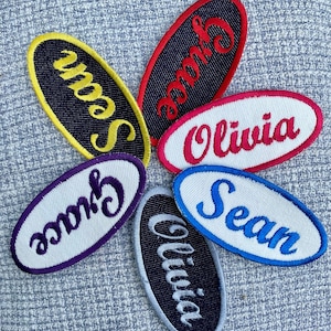 May include: Six oval-shaped fabric patches with embroidered names. The names are "Sean", "Grace", "Olivia", and "Sean". The patches are in various colors, including yellow, red, purple, blue, and black.