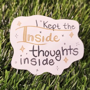 May include: A white sticker with the text "I kept the inside thoughts inside" in black and gold lettering. The sticker has a unique shape and is decorated with small star and diamond shapes.