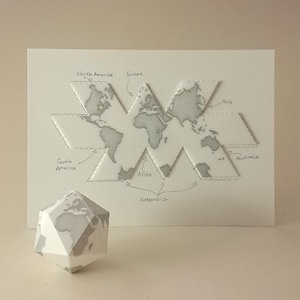 Puede incluir: Un mapa del mundo de papel blanco con continentes grises y etiquetas para América del Norte, Europa, Asia, América del Sur, África, Australia y la Antártida. Un globo geométrico con un diseño de mapa del mundo está frente al mapa.