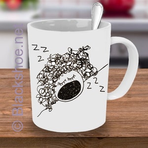 May include: White ceramic mug with a black line drawing of a person with curly hair sleeping with the text "z z z" on the mug.
