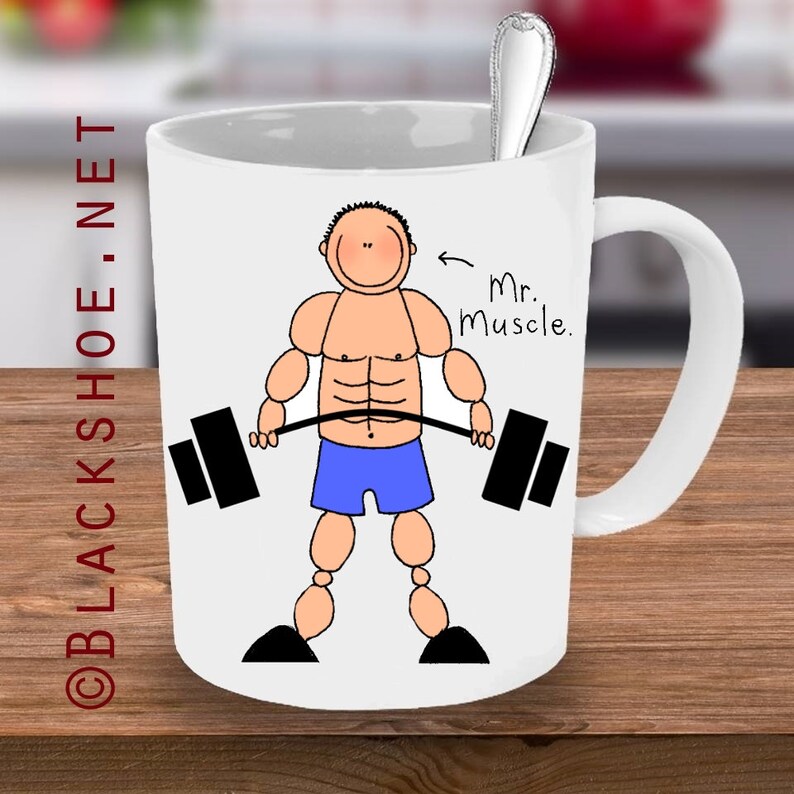May include: White ceramic mug with a cartoon illustration of a muscular person lifting a barbell. The text "Mr. Muscle." is written on the mug.