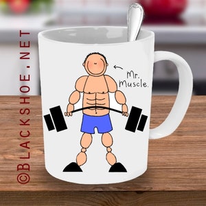 May include: White ceramic mug with a cartoon illustration of a muscular person lifting a barbell. The text "Mr. Muscle." is written on the mug.