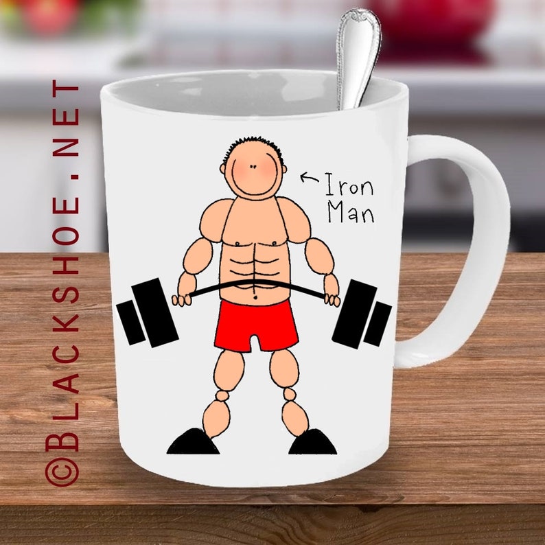 May include: White ceramic mug with a cartoon illustration of a muscular person lifting a barbell. The text "Iron Man" is written next to the person.