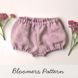 May include: A pair of purple baby bloomers with a gathered elastic waistband. The bloomers are made of a soft, lightweight fabric and have a relaxed fit. The text "Bloomers Pattern" is written below the bloomers.