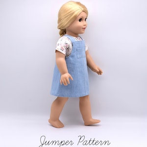 Op de afbeelding: Een pop met blond haar in een zijvlecht, gekleed in een lichtblauwe spijkerjurk over een wit T-shirt met korte mouwen en een klein roze en groen bloemenpatroon. De tekst Jumper Pattern staat in het zwart onder de pop afgebeeld.