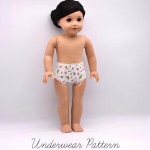 May include: A doll with dark hair styled in a bun, wearing white underwear featuring a small floral print in pink, yellow, and green with delicate white lace trim along the waist and leg openings. The text Underwear Pattern is visible.