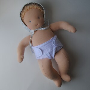 May include: A handmade cloth doll with blonde hair wearing a white diaper and a blue and white patterned bonnet.