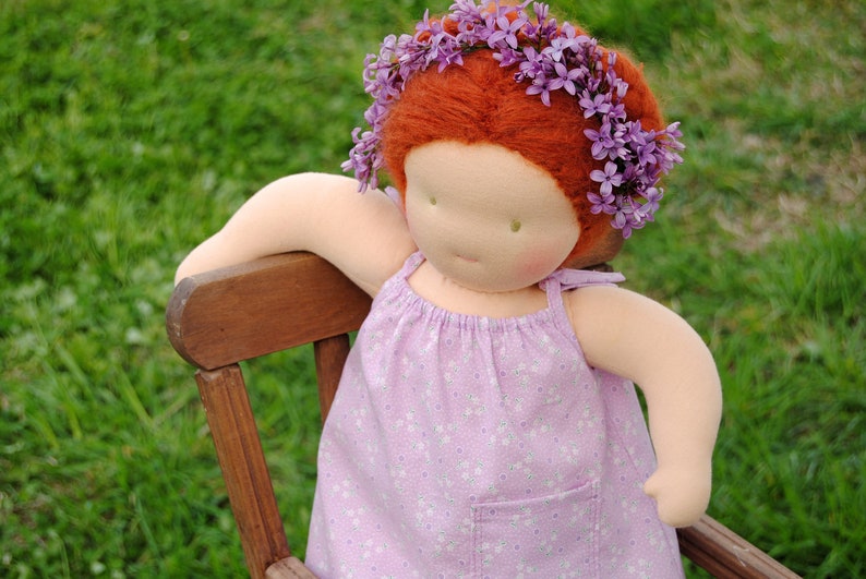 May include: A handmade doll with red hair wearing a purple dress and a flower crown made of purple flowers.