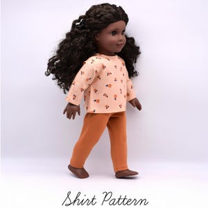 May include: A doll with dark skin and long, curly dark brown hair wearing a long-sleeved, light peach shirt with a small orange floral pattern and solid burnt orange trousers. The text "Shirt Pattern" is printed in black below the doll.