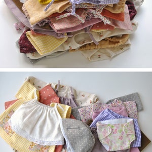 May include: A collection of doll clothes in various colors and patterns, including gingham, floral, and solid colors. The clothes are made of cotton fabric and are suitable for a small doll.