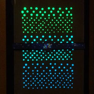 Puede incluir: Una pieza de arte de pared enmarcada en negro con un dise&ntilde;o que brilla en la oscuridad. El dise&ntilde;o presenta un degradado de puntos verdes y azules dispuestos en un patr&oacute;n repetitivo. El texto "STAR SCENES" es visible en la parte inferior del marco.