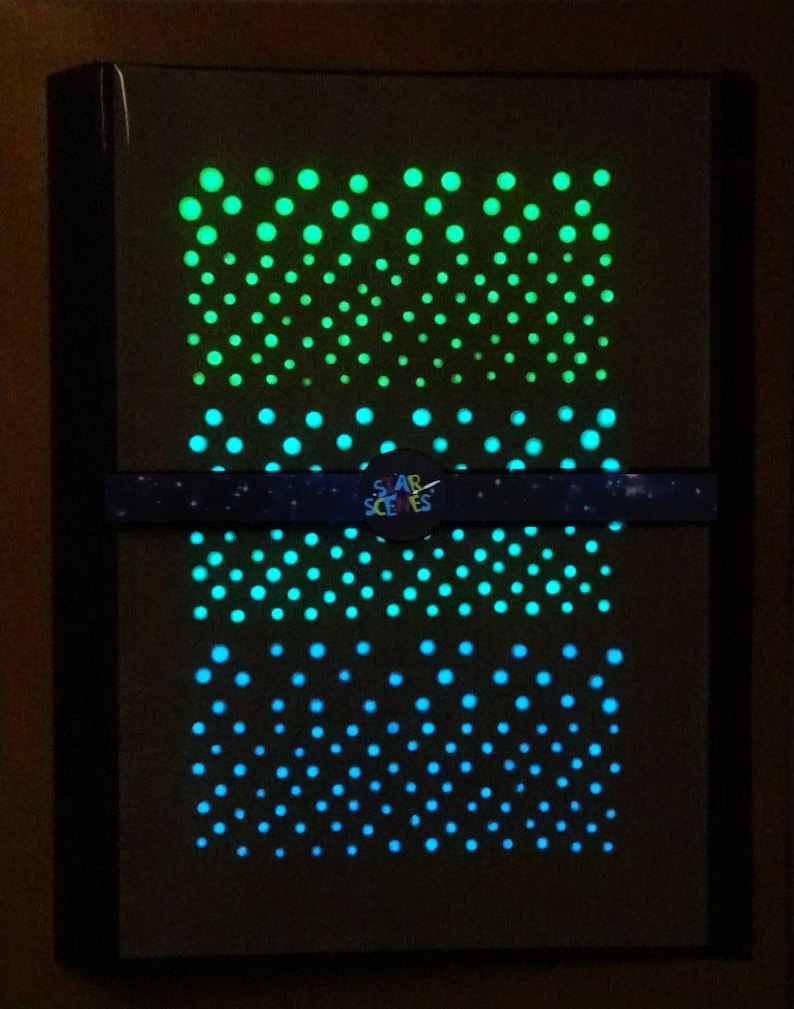 Puede incluir: Una pieza de arte de pared enmarcada en negro con un dise&ntilde;o que brilla en la oscuridad. El dise&ntilde;o presenta un degradado de puntos verdes y azules dispuestos en un patr&oacute;n repetitivo. El texto "STAR SCENES" es visible en la parte inferior del marco.