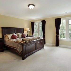 May include: A large, dark wood bed frame with a patterned quilt and two pillows. The bedroom has beige walls, dark wood nightstands, and burgundy curtains.