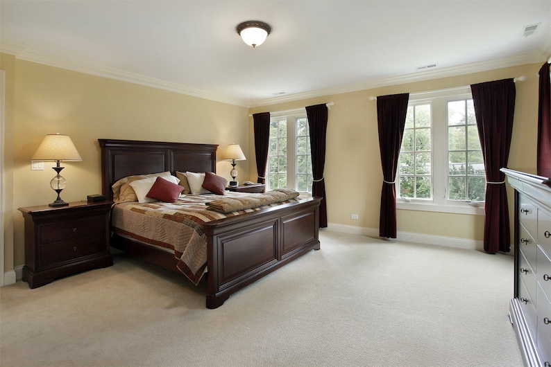 May include: A large, dark wood bed frame with a patterned quilt and two pillows. The bedroom has beige walls, dark wood nightstands, and burgundy curtains.