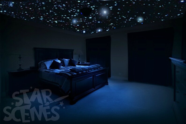 Puede incluir: Un dormitorio oscuro con una cama hecha con almohadas blancas y negras y una manta azul. El techo est&aacute; cubierto con un efecto de cielo estrellado.