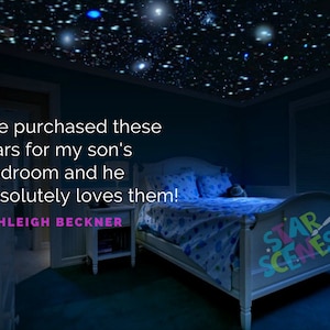 May include: A bedroom with a blue ceiling covered in glowing stars. The bed has a blue and white patterned duvet and a white headboard with the words "STAR SCENES" printed on it. The quote "We purchased these stars for my son's bedroom and he absolutely loves them! ASHLEIGH BECKNER" is in the image.