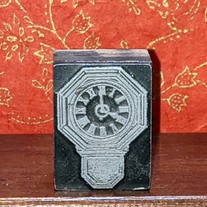 Peut inclure: Un tampon en bois vintage avec une gravure détaillée d'un cadran d'horloge octogonal avec des chiffres romains. Le cadran de l'horloge est gris et les aiguilles sont noires.