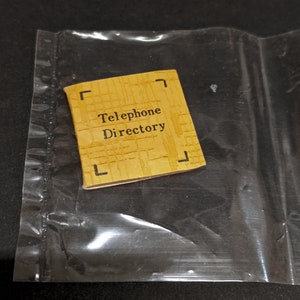 May include: A yellow paper booklet with the text "Telephone Directory" printed in black.