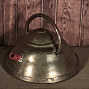 以下が含まれることがあります： 赤いプラスチック製の笛が付いた、小さな銀色の金属製のやかん。やかんは丸みを帯びたドーム型の蓋と、蓋に取り付けられた取っ手があります。