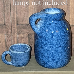 May include: A blue and white ceramic pitcher and a matching cup. The pitcher has a handle and a rounded body. The cup has a handle and a rounded shape. The items are on a wooden surface.
