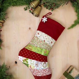 以下が含まれることがあります： 赤い袖口と雪の結晶のチャームが付いた手作りのクリスマスストッキング。ストッキングの本体は、赤、緑、白のデザインなど、さまざまな生地パターンで作られており、「Merry & Bright」と「Let it Snow」のテキストが特徴です。