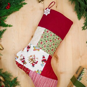 May include: A quilted Christmas stocking featuring a patchwork design with a solid red cuff, a white snowflake ornament, and fabric panels displaying Santa Claus figures, green holly leaves, red berries, and red and white stripes.