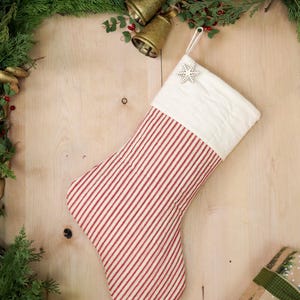 May include: Red and white striped Christmas stocking with a white cuff and a snowflake ornament. The stocking is hanging on a wooden surface.