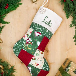 Peut inclure: Une chaussette de Noël matelassée avec un motif patchwork composé de tissu vert à flocons blancs, de tissu rouge et d'un imprimé crème avec des motifs de Père Noël et de cadeaux. Le revers blanc est brodé du prénom Luke et d'un flocon.
