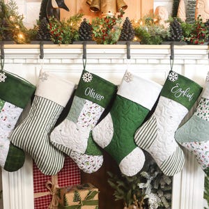 以下が含まれることがあります： 緑と白の色合いのクリスマスストッキングが6つ、マントルピースから吊り下げられています。各ストッキングは、ストライプ、パッチワーク、キルト模様など、ユニークなデザインです。「Oliver」、「Ezekiel」、「Graham」などの名前がパーソナライズされたストッキングもあります。