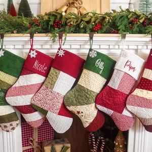 May include: Six quilted Christmas stockings hanging in a row, featuring various patchwork patterns in red, green, cream, and white fabrics. Some stockings are personalized with embroidered names including Nicole, Olly, and Piper in white script.