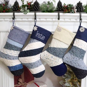 以下が含まれることがあります： 白い暖炉の棚に、雪の結晶の飾り物がついた青と白のストライプのクリスマスストッキングが4つ掛かっています。1つのストッキングには「トリスタン」という名前が書かれています。