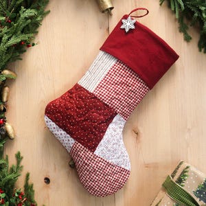 Pode incluir: Uma meia de Natal artesanal com punho vermelho e um pingente de floco de neve. O corpo é um patchwork de tecidos estampados em vermelho e branco, incluindo xadrez e bolinhas. Uma decoração festiva.