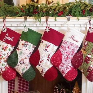 May include: Five quilted Christmas stockings hanging in a row, featuring varied festive patterns of Santa Claus, reindeer, and trees in red, green, and white. Two stockings are personalized with the embroidered names Jacob and Haven in white script.
