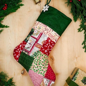 Könnte beinhalten: Ein Patchwork-Weihnachtsstrumpf mit dunkelgrünem Umschlag und einem weißen Schneeflocken-Ornament. Der Körper zeigt verschiedene Stoffmuster, darunter rot-weiße Punkte, rotes Vichy-Karo, Stechpalmenblätter und weihnachtliche Schriftzüge.