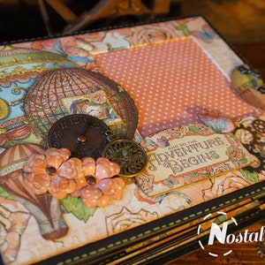 Peut inclure: Album de scrapbooking décoratif sur le thème du voyage vintage. La couverture présente des illustrations de montgolfières, des ornements d'horloge et la phrase « And So The Adventure Begins ». L'album a un motif pêche et floral avec une bordure noire.