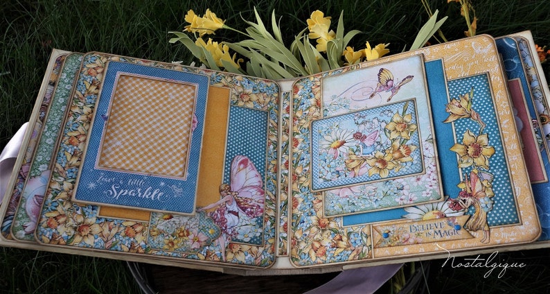 K&ouml;nnte beinhalten: Ein offenes Scrapbook mit einem floralen Design mit gelben Narzissen, Schmetterlingen und dem Text "Glaube an die Magie". Das Scrapbook hat mehrere Taschen und Rahmen f&uuml;r Fotos und Verzierungen.