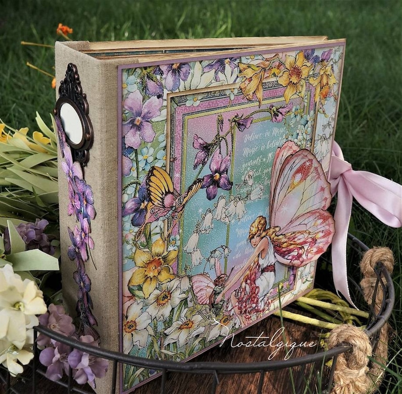 K&ouml;nnte beinhalten: Ein Scrapbook mit einem floralen Design, das eine Fee mit Fl&uuml;geln, Blumen und dem Text "Glaube an Magie, wo ist besser, lass einfach deine Fantasie fliegen" zeigt.