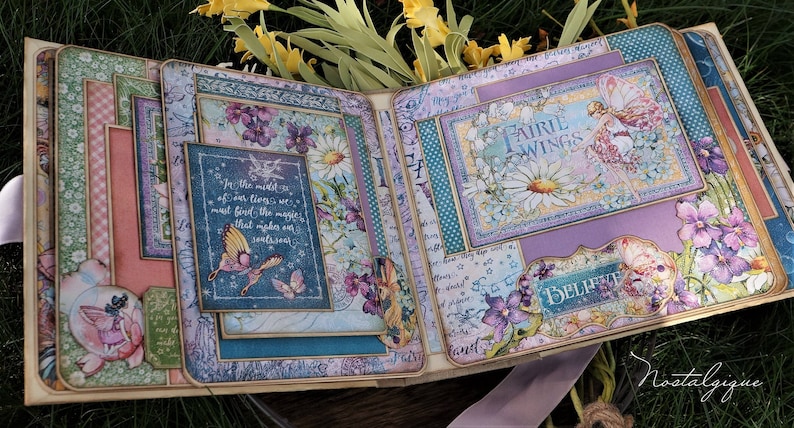 K&ouml;nnte beinhalten: Ein Scrapbook mit einem violetten, blauen und gr&uuml;nen Blumendesign. Das Scrapbook ist ge&ouml;ffnet und zeigt eine Seite mit einem Zitat &uuml;ber das Finden von Magie inmitten des Lebens. Die Seite zeigt auch eine Fee mit Fl&uuml;geln und eine G&auml;nsebl&uuml;mchen.