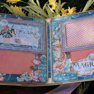 K&ouml;nnte beinhalten: Eine Scrapbook-Seite mit blauem und rosa Farbschema, die Feen, Blasen und den Text "Lass deine Tr&auml;ume fliegen" und "Finde die Magie, die deine Seele zum Leuchten bringt" zeigt.