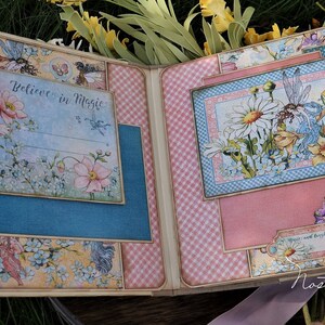 K&ouml;nnte beinhalten: Ein Scrapbook mit einem rosa-blauen Karomuster. Der Vorderdeckel zeigt ein florales Design mit einer Fee und dem Text "Glaube an Magie". Der Hinterdeckel zeigt ein florales Design mit einer Fee und dem Text "Tr&auml;ume".