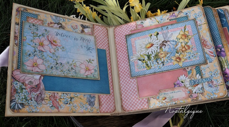 K&ouml;nnte beinhalten: Ein Scrapbook mit einem rosa-blauen Karomuster. Der Vorderdeckel zeigt ein florales Design mit einer Fee und dem Text "Glaube an Magie". Der Hinterdeckel zeigt ein florales Design mit einer Fee und dem Text "Tr&auml;ume".