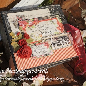 Può includere: Un album di scrapbook decorativo a tema musicale. L'album presenta rose rosse, spartiti e la citazione "La musica è il silenzio tra le note". Un nastro rosso accentua il design. L'album è decorato con carta e abbellimenti in stile vintage.