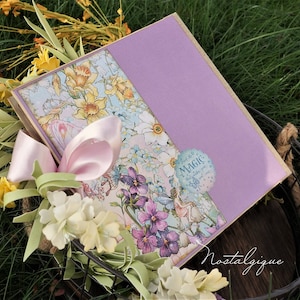 K&ouml;nnte beinhalten: Ein lilafarbener und floral verzierter Scrapbook mit einem rosa Band und einem Aufkleber mit der Aufschrift "Finde die Magie" auf dem Einband. Der Scrapbook liegt in einem Drahtkorb mit gelben Blumen.
