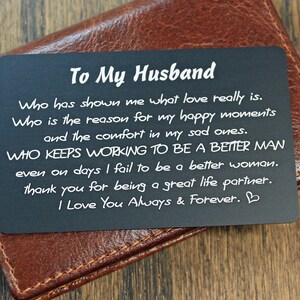 May include: A black metal card with white text that reads "To My Husband" and a message about love and appreciation. The card is sitting on a brown leather wallet.