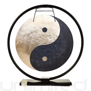 May include: A Yin and Yang gong with a black frame and stand. The gong is divided into two sections: a silver-colored side and a dark blue side. The gong is suspended within a circular frame, and a mallet rests on the stand.