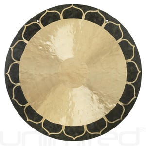 May include: A large, circular gong with a polished brass center and a dark, patterned border. The border features a repeating floral design in a lighter color. Two small holes are visible near the top edge.