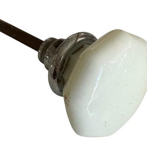 May include: A vintage white porcelain door knob with a chrome base and a rusty brown metal rod. The knob has a rounded, rectangular shape and shows signs of age.